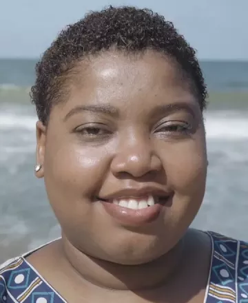 Mulher negra sorrindo para a foto enquanto está em uma praia
